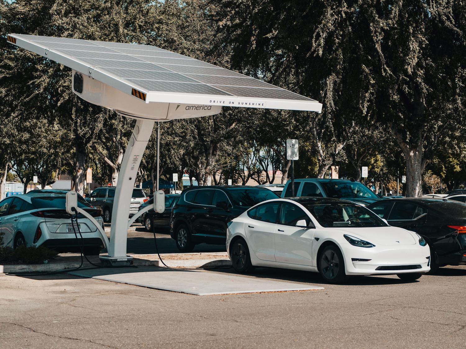 Coche eléctrico cargando en una estación con paneles solares, destacando la sostenibilidad y la energía renovable.