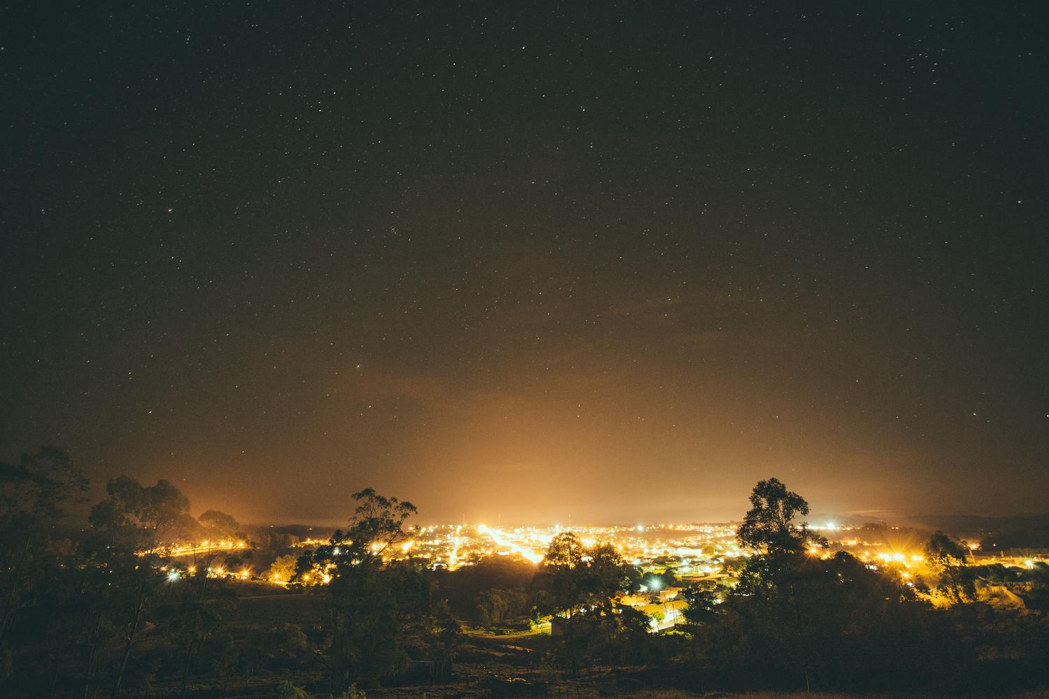 Contraste entre un cielo estrellado profundo y la cúpula de luz artificial que envuelve un asentamiento urbano, mostrando el gradiente de oscuridad.