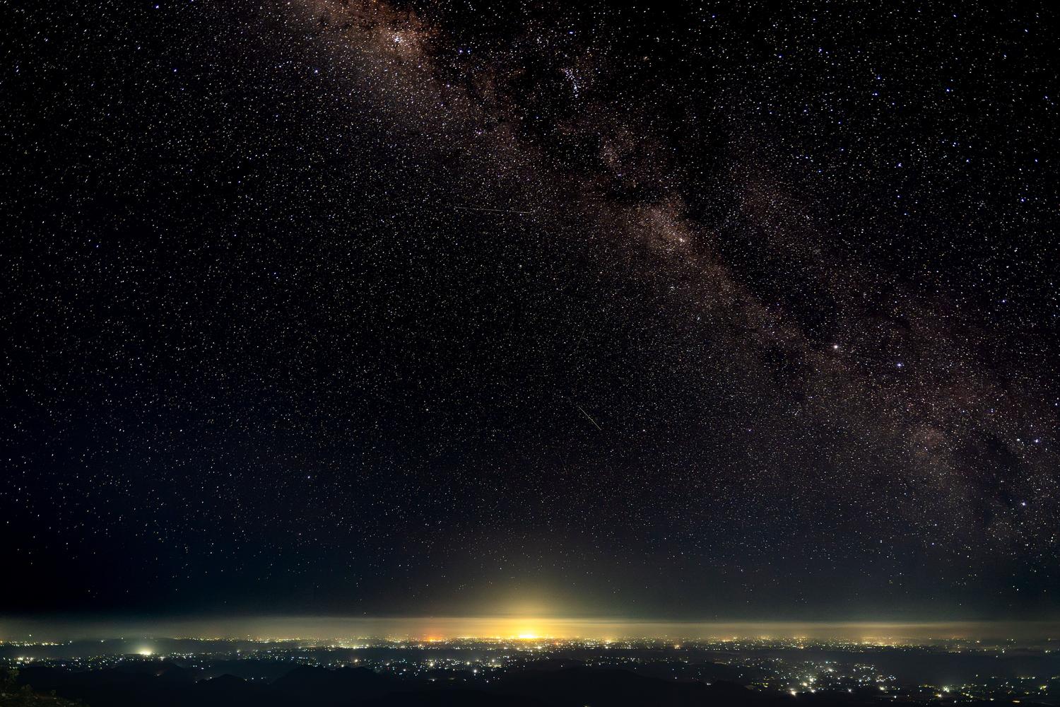 La Vía Láctea visible sobre el horizonte, donde se aprecia la contaminación lumínica de una ciudad distante en el fondo.