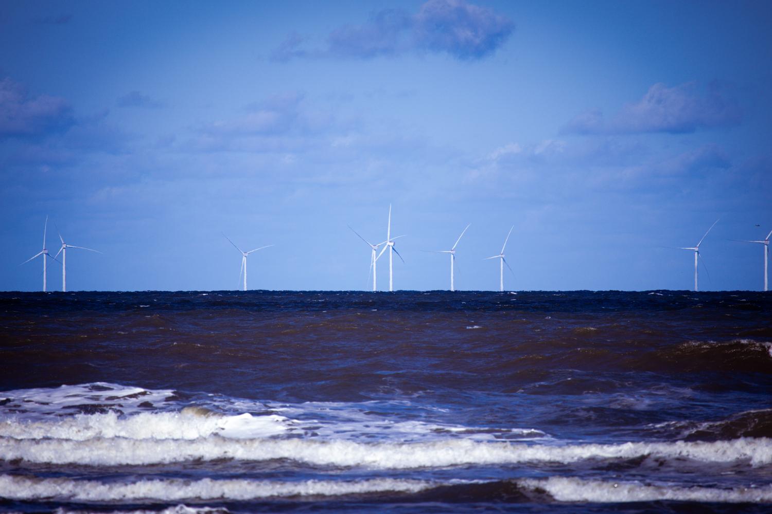 Aerogeneradores marinos generando energía sostenible en el océano bajo un cielo despejado.