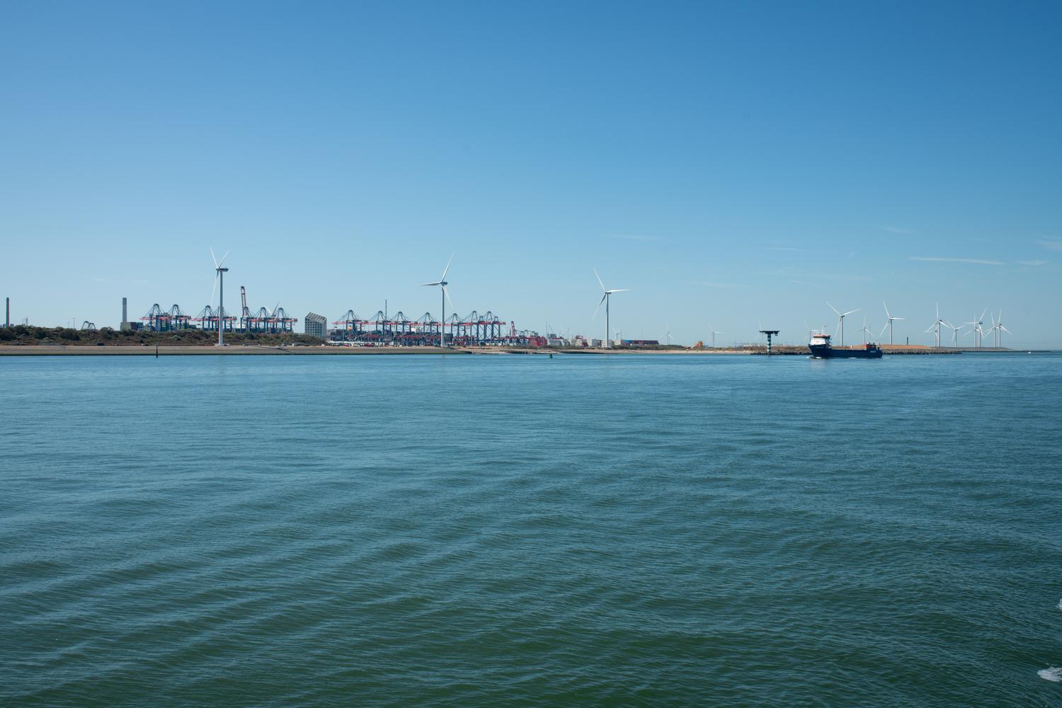 Vista de un parque eólico costero junto a un puerto de embarques, integrando energía renovable y actividad marítima. Vista de un parque eólico costero junto a un puerto de embarques, integrando energía renovable y actividad marítima.