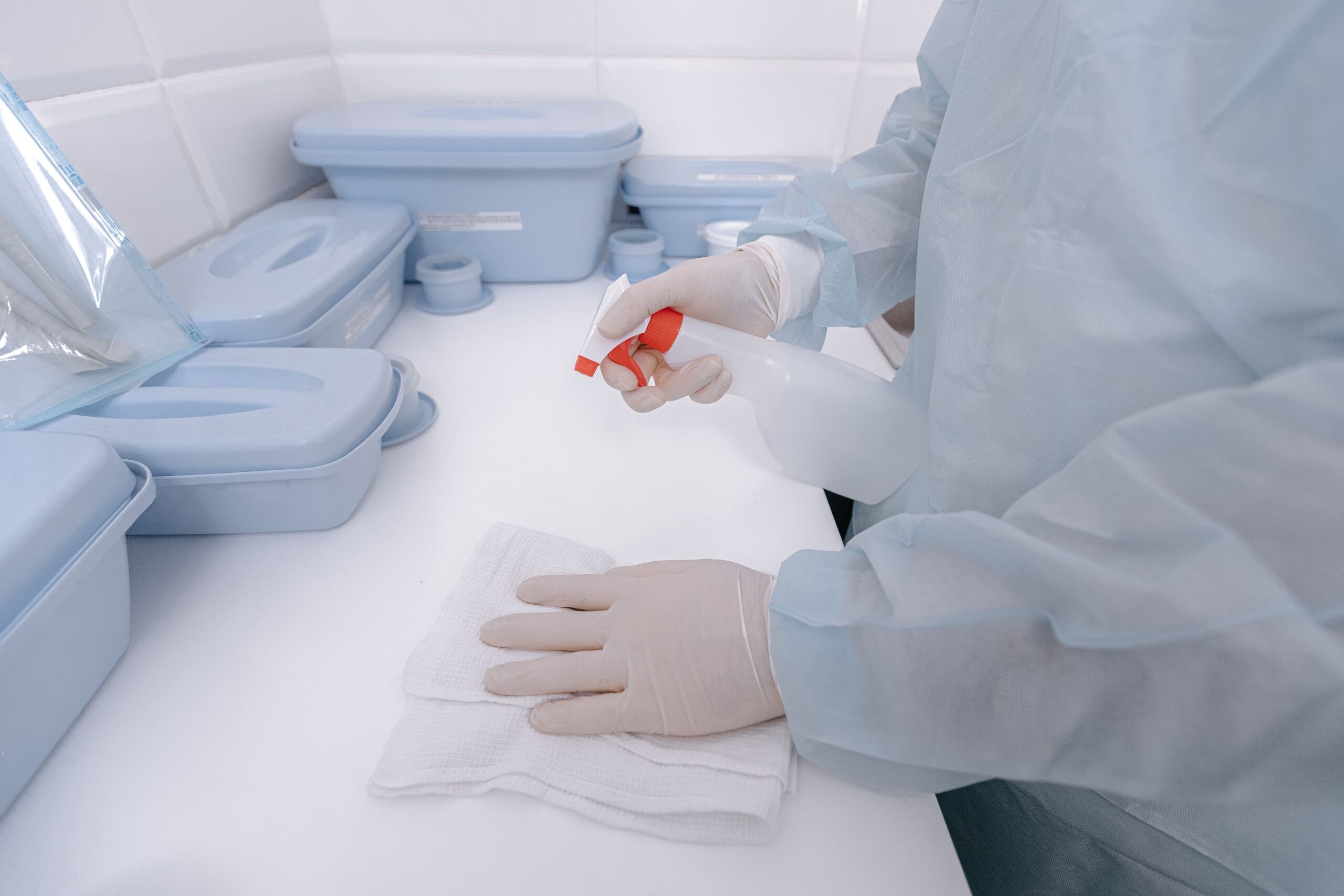 Profesional de la salud con guantes desinfectando una superficie mediante la pulverización de agentes químicos.