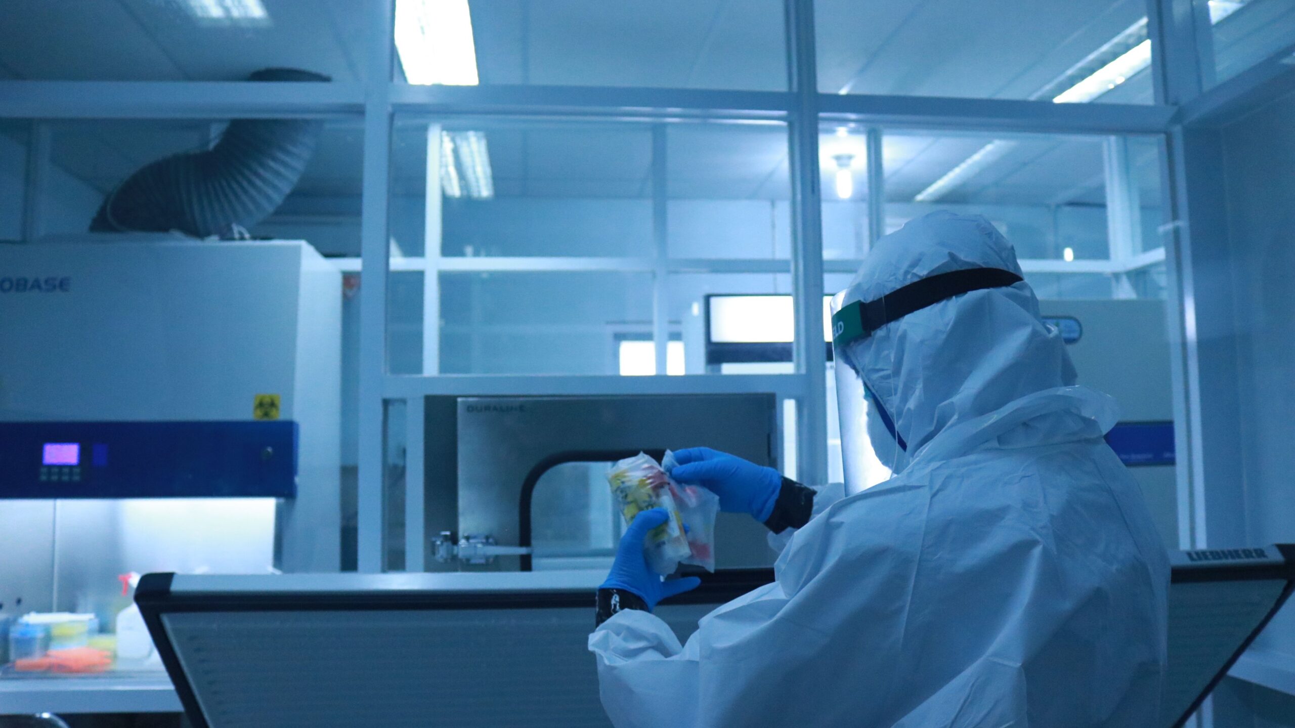 Técnico de laboratorio con traje de protección completa realizando tareas de control y validación en un entorno controlado.