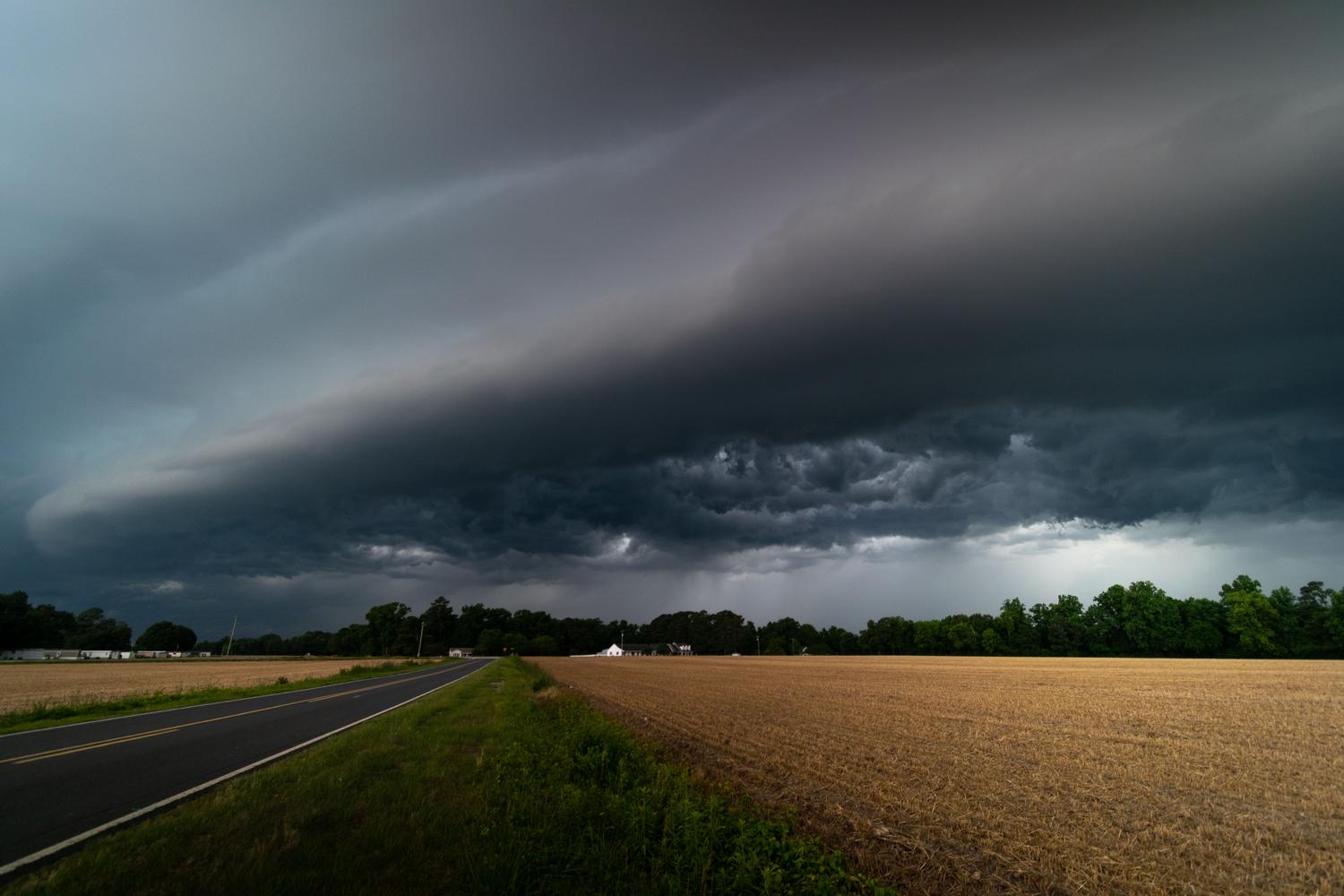Nubes oscuras de tormenta aproximándose a una carretera rural, representando el riesgo de los reventones húmedos.