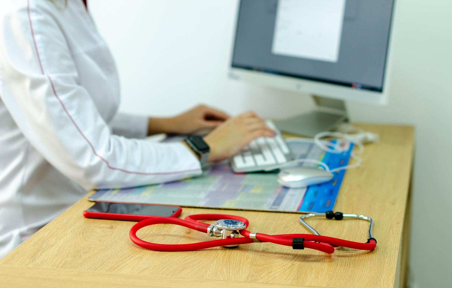 Profesional médico con ordenador y estetoscopio, simbolizando la unión entre la tecnología digital y el razonamiento clínico.