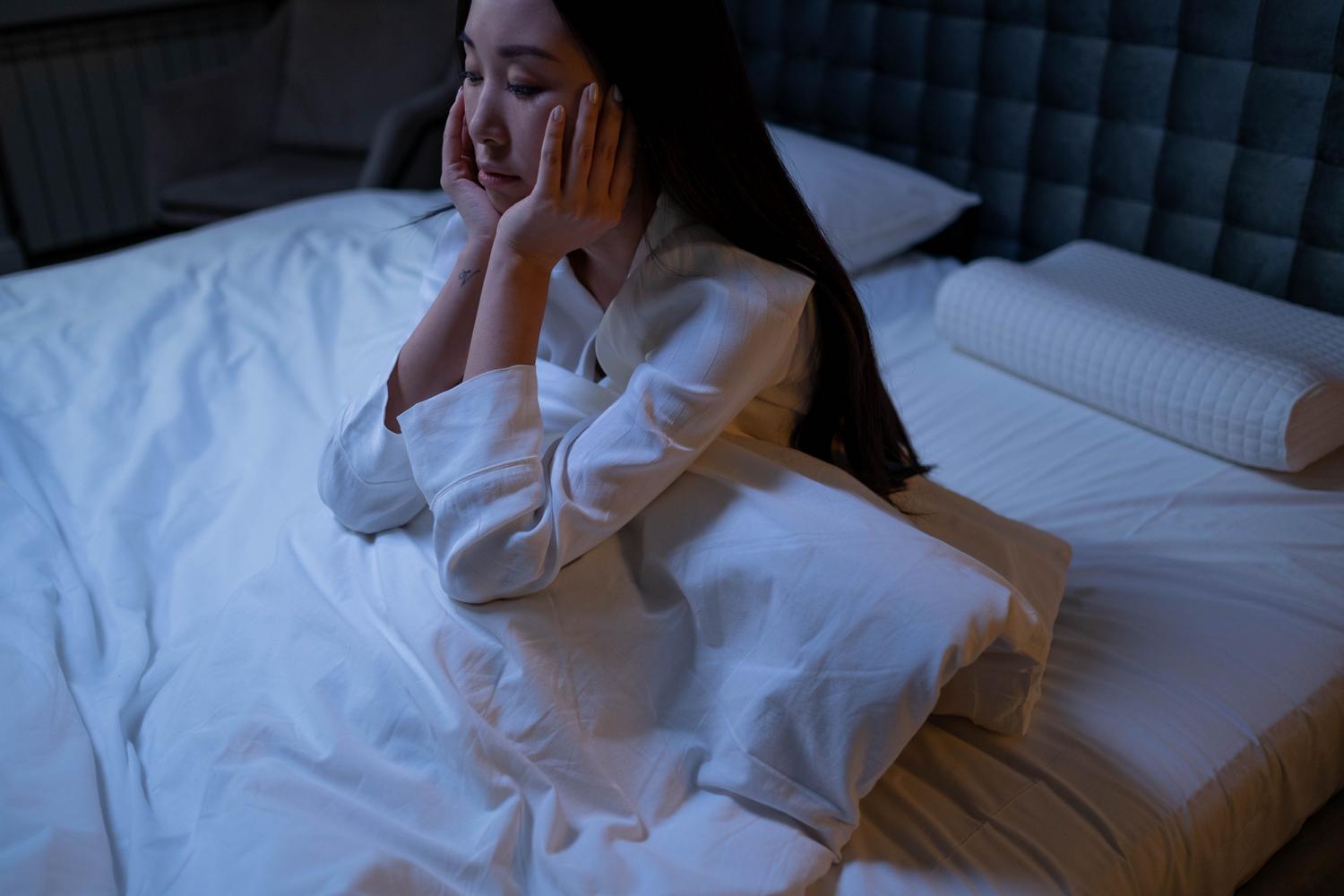 Mujer sentada en la cama con expresión de angustia y soledad debido al insomnio crónico.