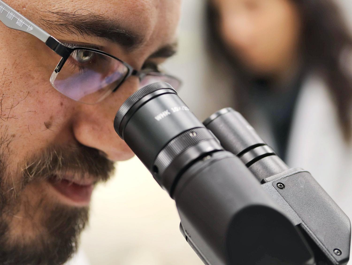 Científico analizando muestras bajo un microscopio de alta precisión, representando la especialización en ciencia de materiales y biomateriales.
