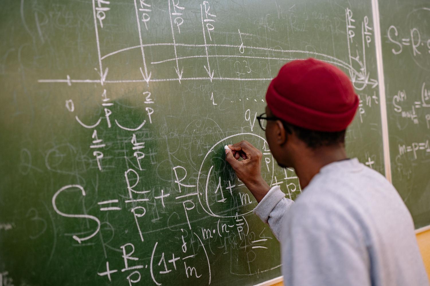 Estudiante escribiendo ecuaciones matemáticas complejas en una pizarra, simbolizando el rigor científico y la formación de nuevas generaciones de físicos.