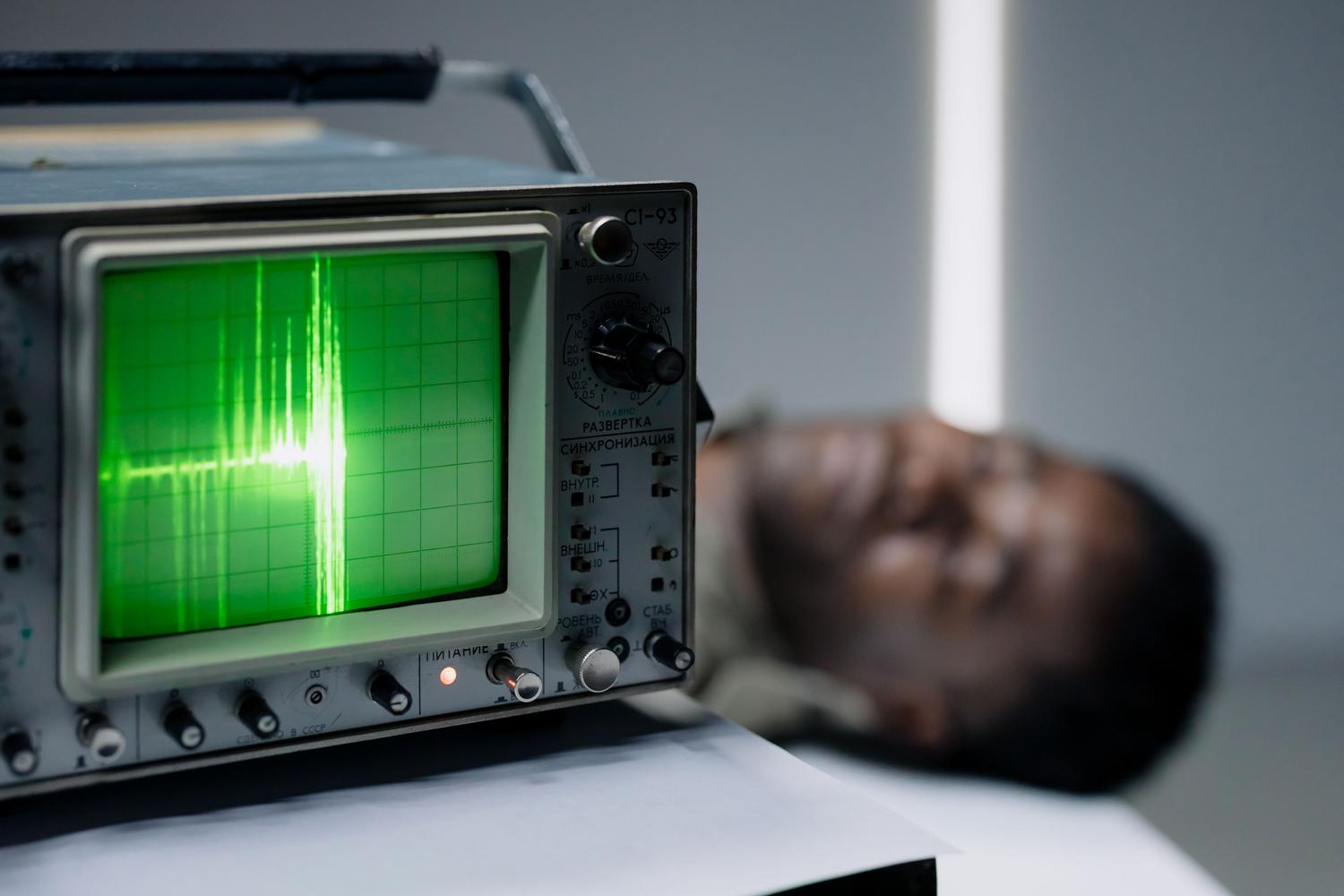 Primer plano de la pantalla de un osciloscopio analógico mostrando una señal eléctrica en forma de onda verde sobre una cuadrícula.