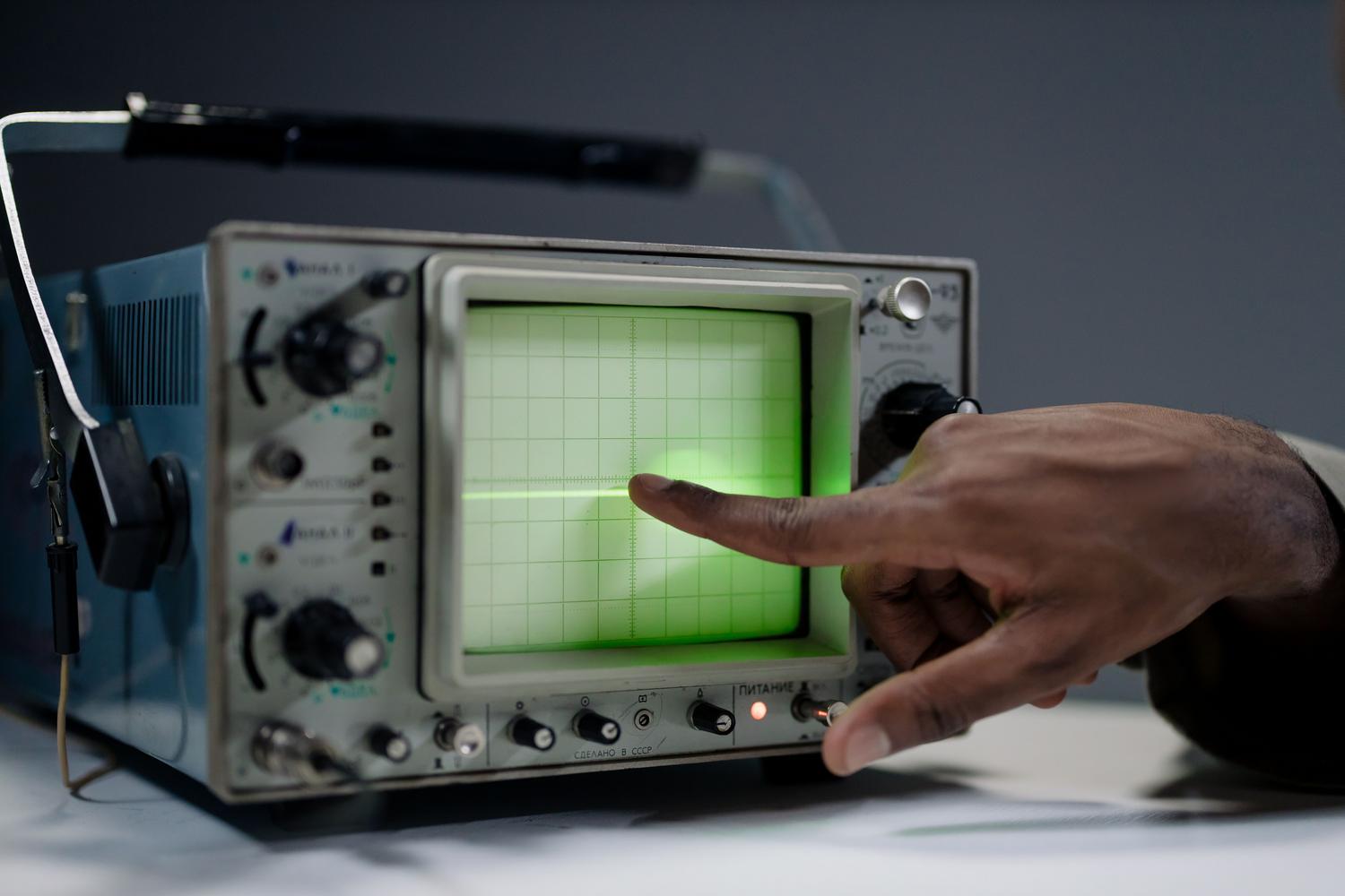 Mano de un técnico señalando la pantalla de un osciloscopio vintage para analizar la respuesta de un sistema electrónico.