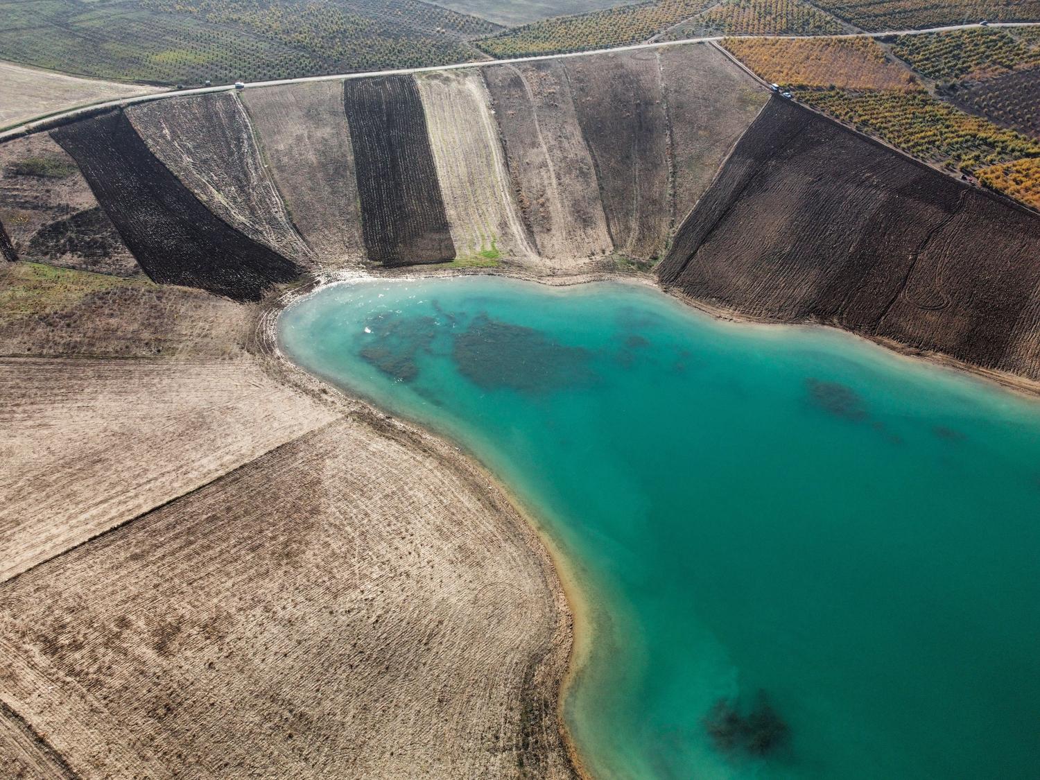 Vista aérea de campos de cultivo junto a un lago turquesa, ilustrando la relación entre el agua subterránea y los ecosistemas superficiales.