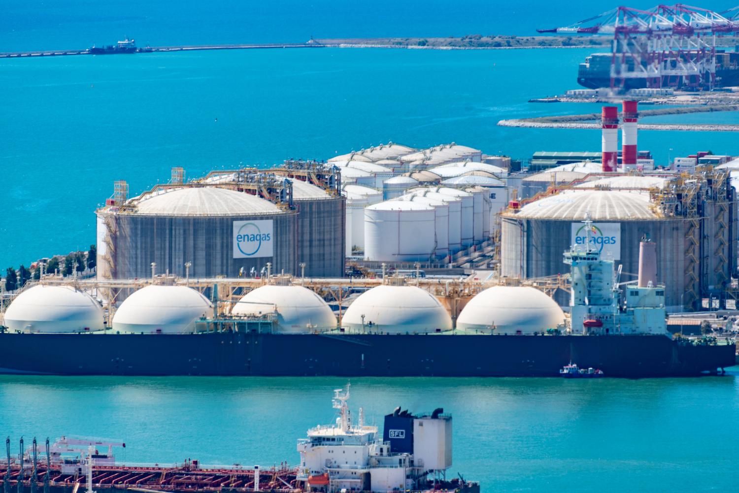 Vista aérea de una terminal de GNL con grandes tanques de almacenamiento blancos y buques metaneros en aguas turquesas